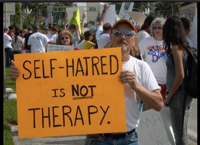 Protester holds a sign that reads: "self-hatred is not therapy."